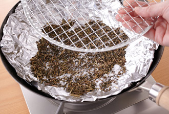 中華鍋（または深さのある鉄のフライパン）にアルミホイルを敷き、茶葉、砂糖をまんべんなく敷いて焼き網をのせる。