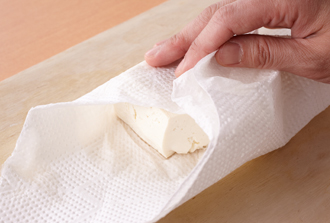 豆腐をペーパータオルで包んでぎゅっとつぶす。ペーパータオルを替えてさらに2回ほどつぶして水気をしっかりきり、ボウルに入れる。