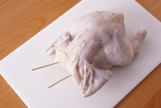 鶏肉の表面、腹の中全体ににんにく、たっぷりの塩、黒こしょうをもみ込む。首のまわりの皮をひっぱって穴を閉じ、竹串で留める。