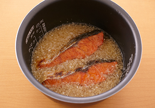 炊飯器の内釜に米と酒を入れ、2合の目盛りまで水を注ぎ入れる。Aを加えて混ぜ、焼いた鮭をのせて炊く。