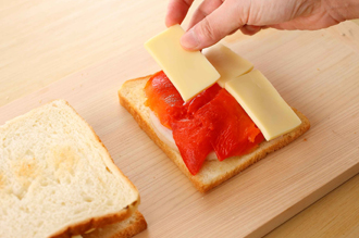 食パンはトーストし、片面に練り辛子とバターを塗る。塗った面を上にして、ハム、パプリカ、チーズの順にそれぞれ1/6量ずつのせ、もう1枚のトーストをのせてはさむ。残りも同様にしてはさむ。