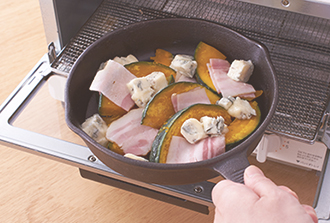 スキレット（または耐熱の器）にかぼちゃを並べ、ベーコンをのせてチーズを散らす。オーブントースター（1000W）で5分ほど焼き、チーズがとけたらでき上がり。黒こしょうをふり、はちみつをかける。