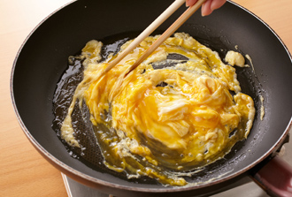 チャーハンを作る。ボウルに卵を溶きほぐし、塩少々を加える。ねぎはみじん切りにする。ベーコンは幅2センチに切る。フライパンにごま油を強火で熱し、溶き卵を流し入れる。大きく混ぜ、ふわっと半熟状になったら一度取り出す。