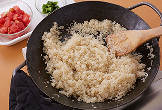 同じパエリアパンにオリーブ油大さじ1/2を足し、玉ねぎ、にんにくを入れて中火で3分ほど炒める。米を洗わずに入れて1分ほど炒め、表面がつやつやになったらトマト、ピーマンを加えて炒める。