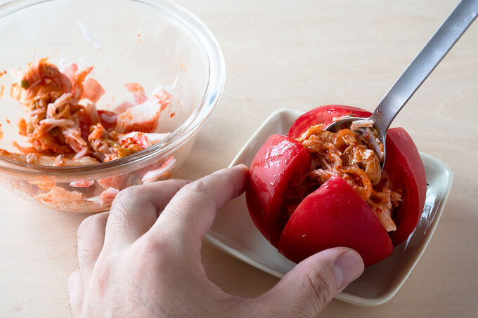 かにかま、白菜キムチを粗く刻んで混ぜ合わせ、トマトの切り込みに入れる。ごま油、塩をかける。