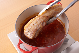 沸騰したら塩小さじ1と1/2、水を加えて混ぜ、豚肉を戻し入れる。ふたをして、弱火で30～40分、汁気が1/3量くらいになるまでときどき上下を返しながら煮て豚肉を取り出す。鍋の煮汁に塩、黒こしょう少々を加えて味をととのえ、ソースとして器に敷く。豚肉を食べやすく切って皿に盛る。好みの葉野菜を飾る。