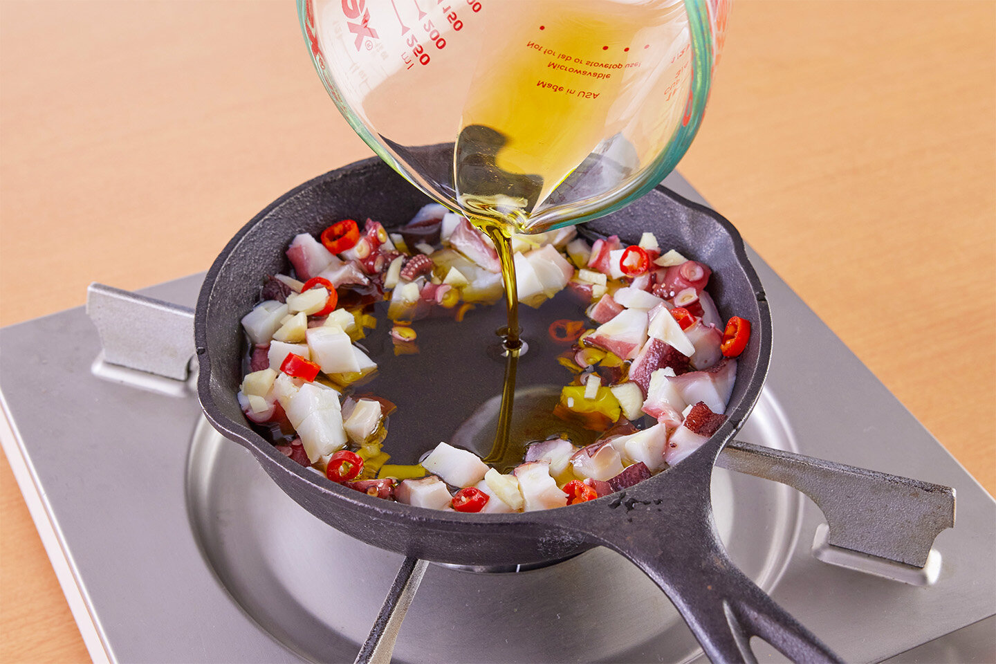 スキレットにゆでだこ、にんにく、赤唐辛子を入れて混ぜる。<br>中央を空けて、オリーブ油を注ぎ入れる。中火にかけ、2分ほど煮る。