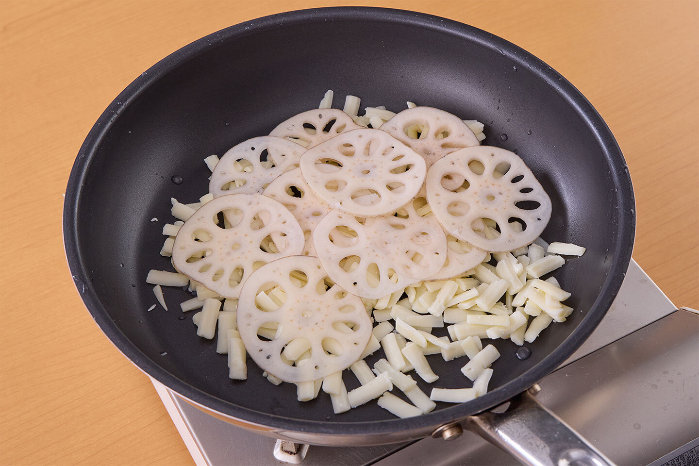 フライパンにピザ用チーズを広げ、れんこんをできるだけ重ならないように並べる。弱めの中火にかけて5分ほど焼く。チーズがこんがりしたら上下を返し、さらに2分ほど焼く。ざるにのせて冷まし、食べやすい大きさに切る。