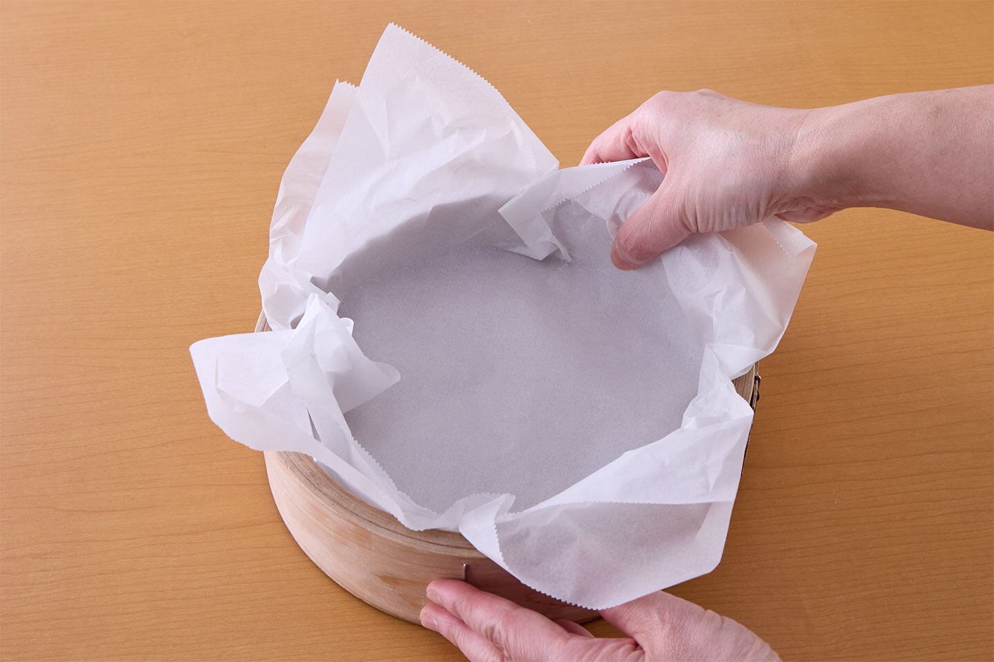 オーブン用シート（クッキングシート）を2枚、大きく切り、せいろ（内径18㎝）に重ねて入れ、すみまで敷きつめる。