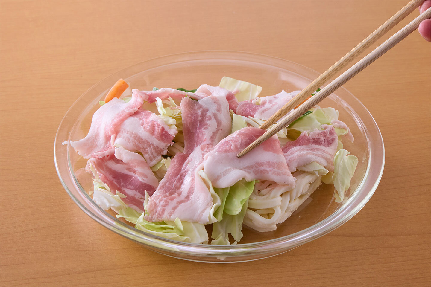 耐熱皿の中央に冷凍うどんを凍ったままのせ、その上にカット野菜をのせ、豚肉は重ならないよう広げてのせる。Aを全体に回しかける。