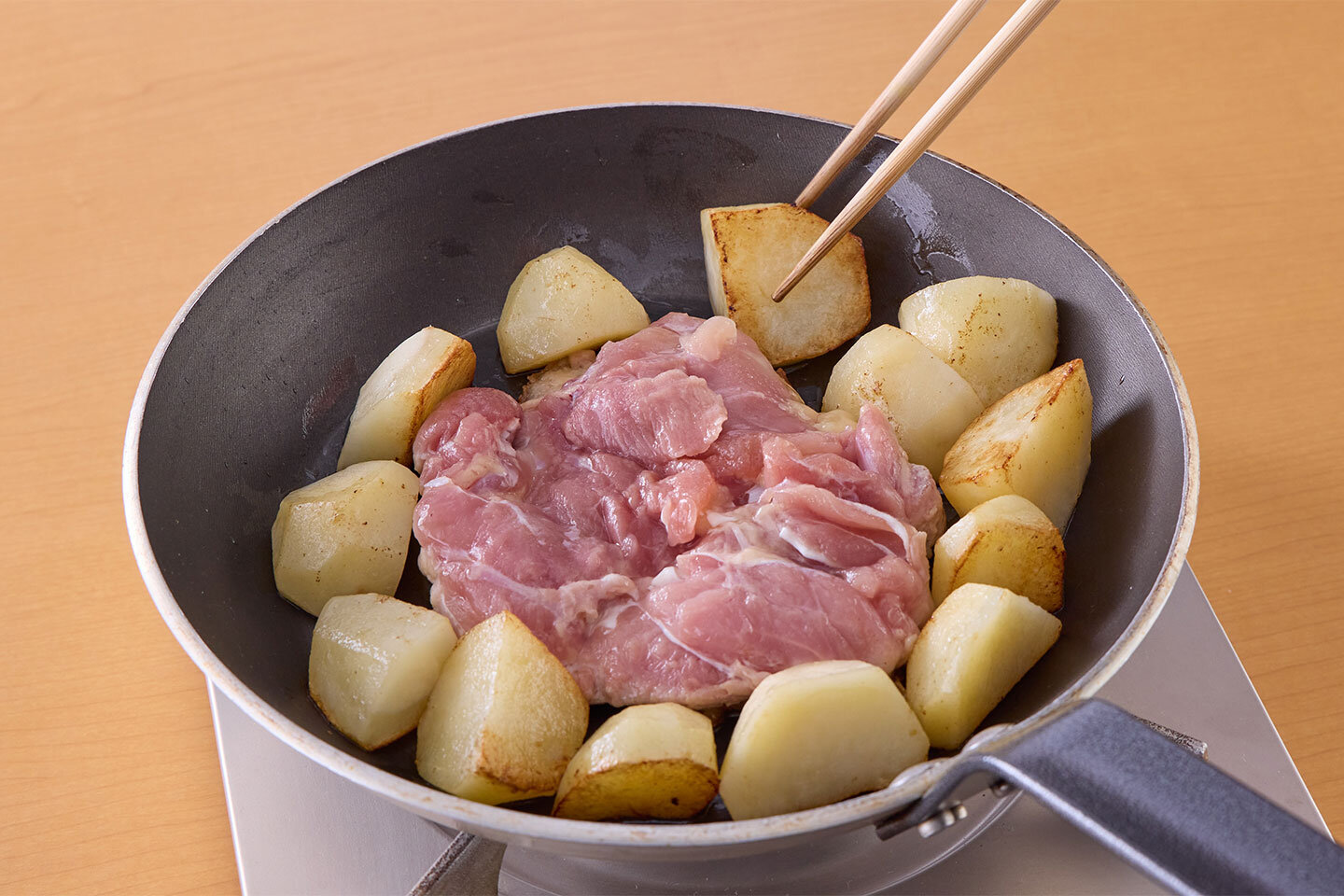 フライパンにオリーブ油を入れ、鶏肉の皮を下にして入れる。あいている場所にじゃがいもの断面を下にして並べる。中火にかけ、7〜8分焼く。鶏肉の上下を返し、玉ねぎ、にんにくを加えて、中火で3分ほどじゃがいもとともに炒める。