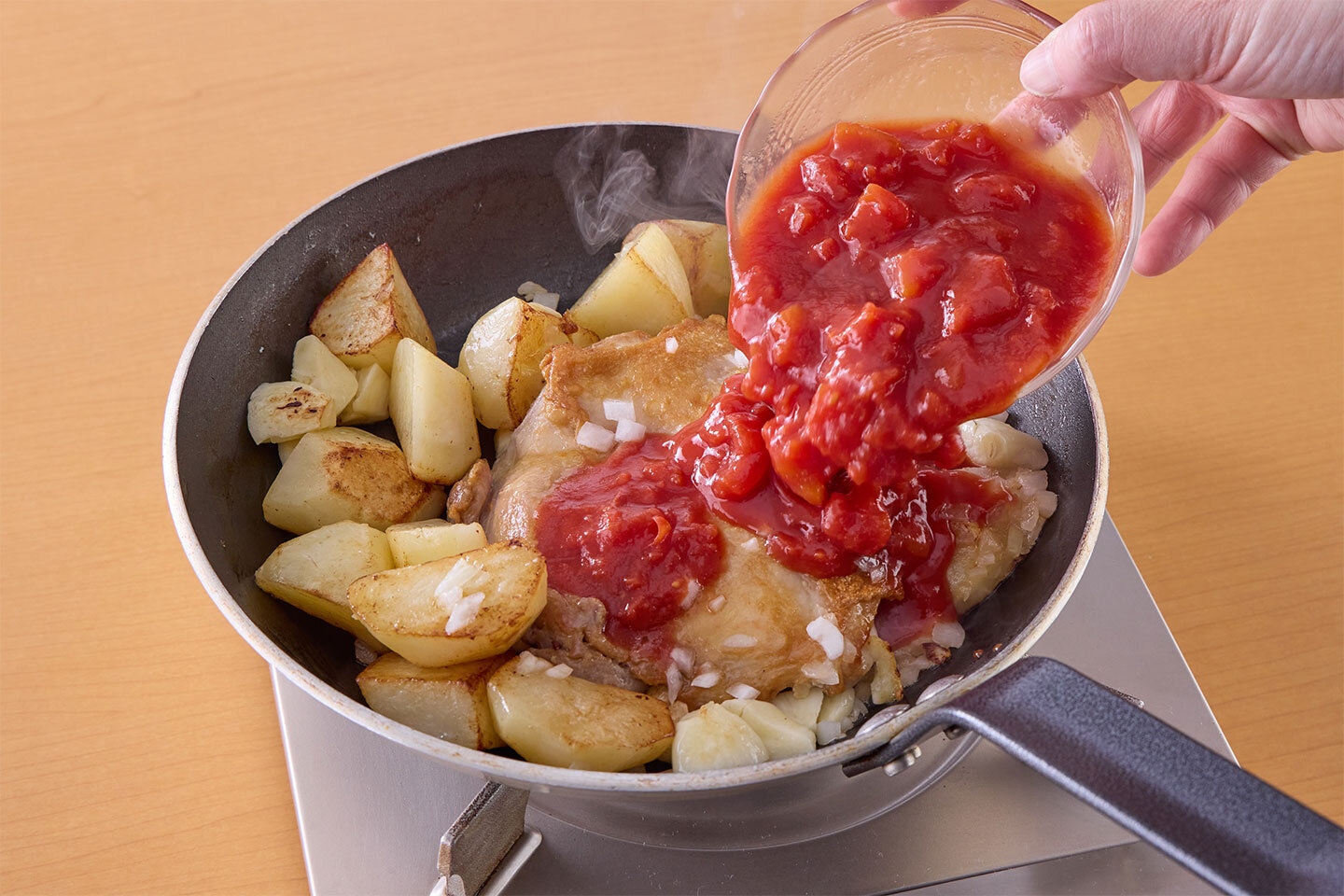 トマトの水煮を加える。空いた缶にワインを注いで、缶の中をゆすぎながらトマトの水煮の缶汁と共にフライパンに加え、蓋をせずに中火で7〜8分ほど煮る。塩小さじ1/3を加えて味をととのえる。火が通ったら、最後にバジルを散らし、鶏肉は食べる時に食べやすく切る。