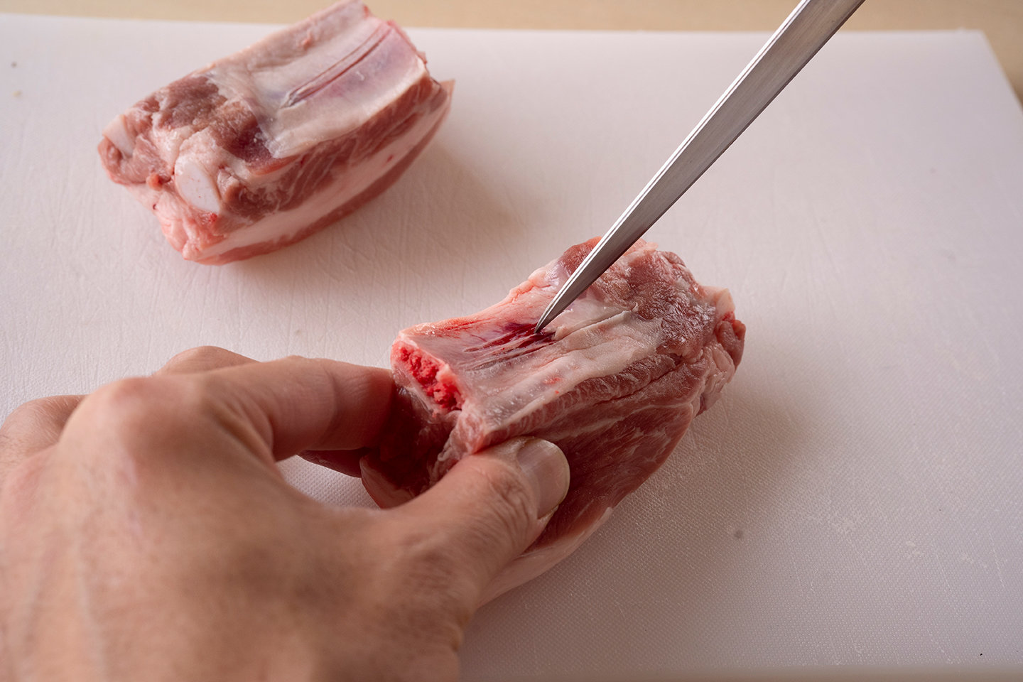 スペアリブは骨の上の薄い皮に、包丁で２〜３回切り込みを入れる。こうすると、肉と骨がはがれやすくなる。